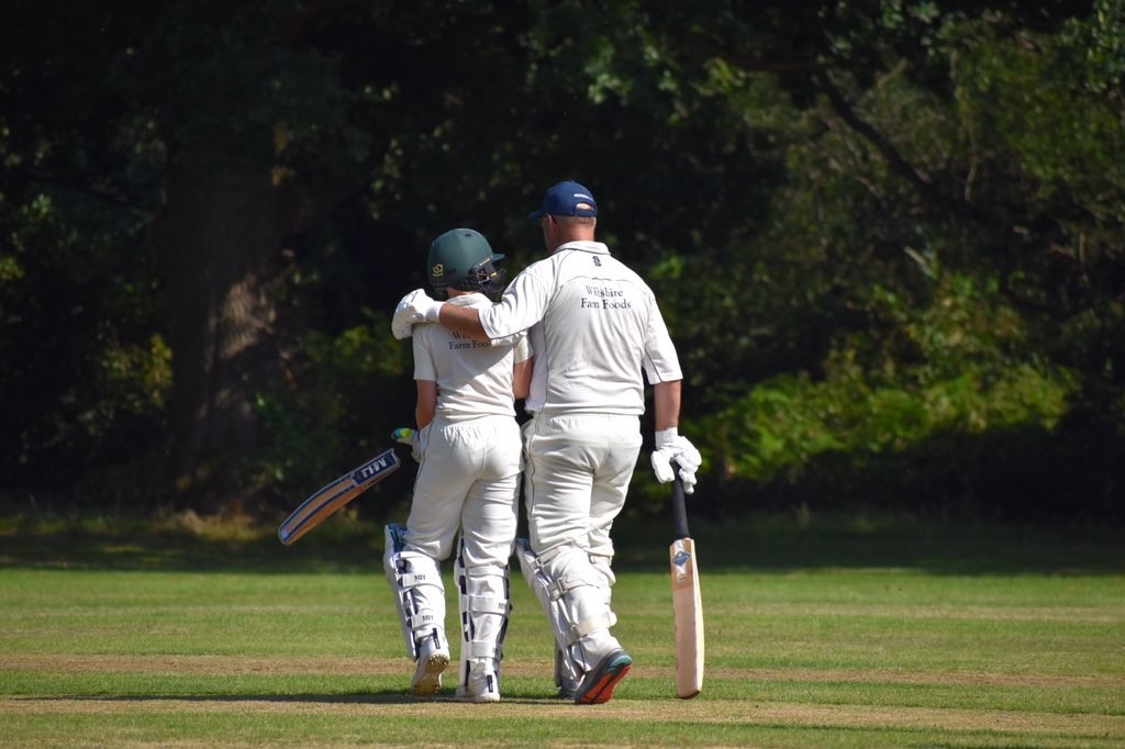 Young person and older man walking away from camera in cricket whites