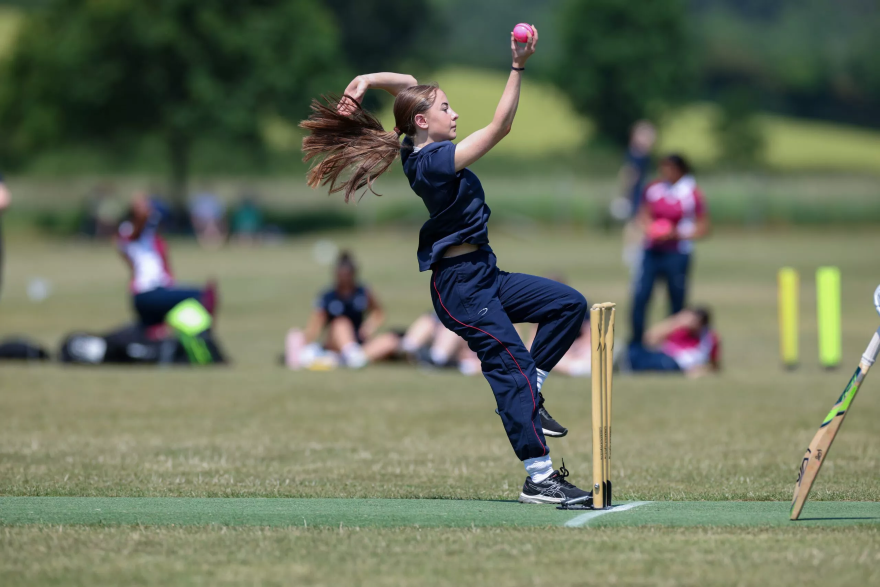 Young girl in motion bowling a cricket ball on a green