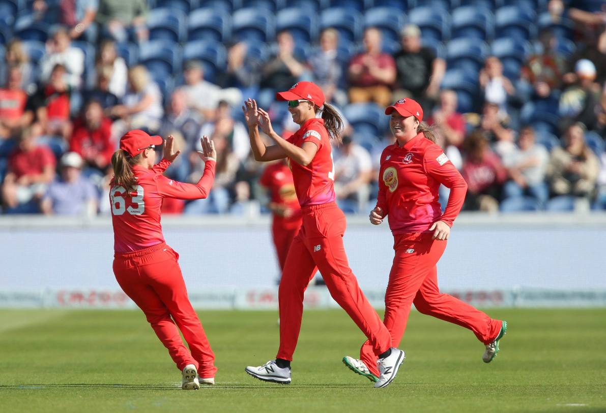 Welsh Fire women's cricket team high-fiving on pitch with blurred crowd in background