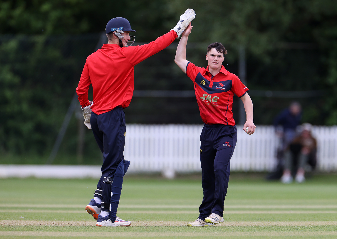 Two young men in Cricket Wales kit high-fiving on a cricket pitch