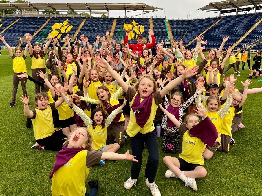 Group of girls in yellow kit raising arms and shouting at the camera joyfully