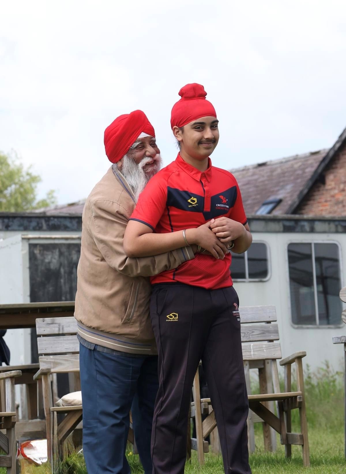 Older man embracing a younger boy in Cricket Wales kit